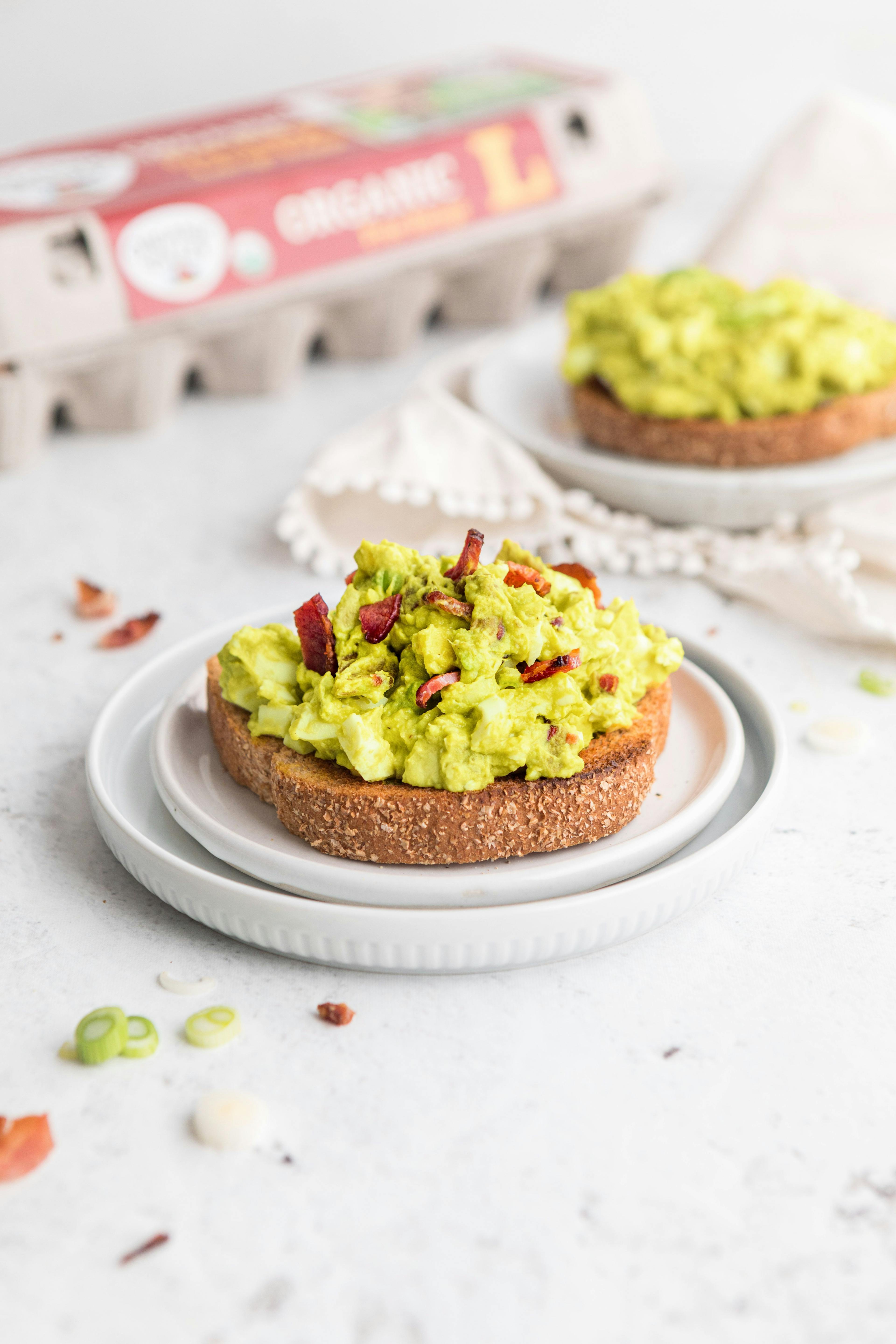 A piece of toast with Avocado Egg Salad with Bacon on top