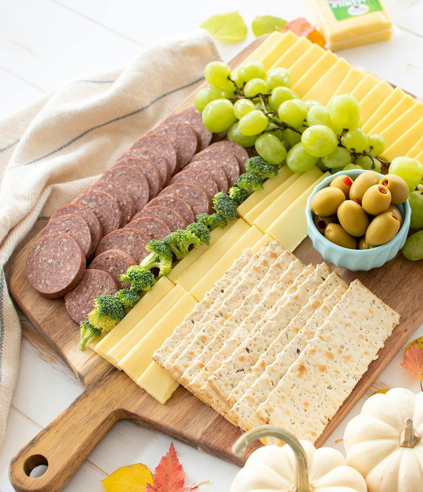 A charcuterie board with sausage, cheese, fruits, vegetables, and crackers.