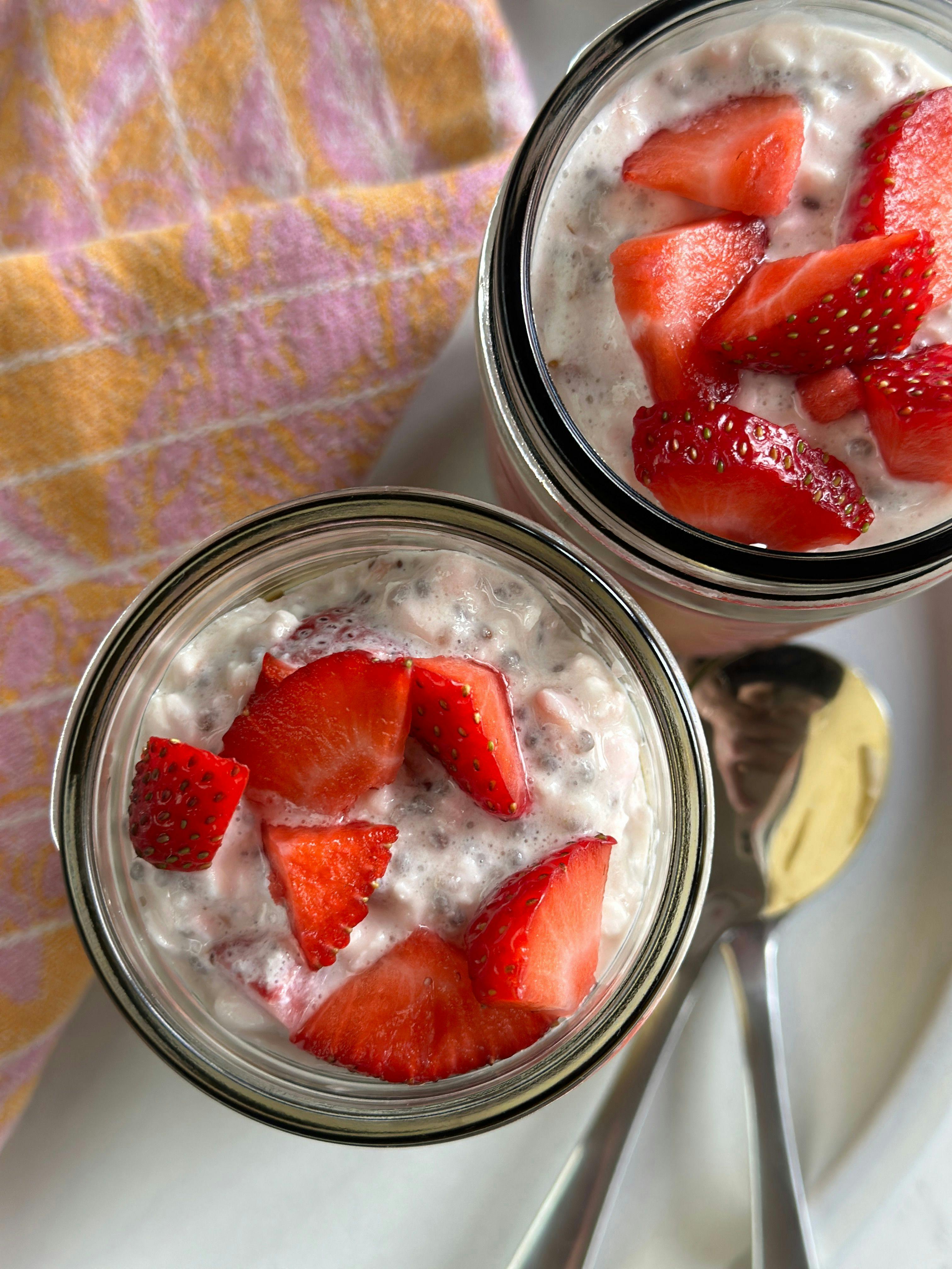 Strawberry Cottage Cheese Chia Cups in two glass jars and a spoon next to it. 