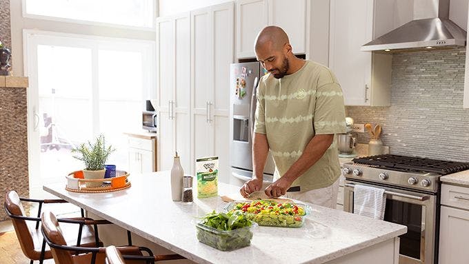 Man preparing salad in kitchen with Organic Valley shredded cheese.