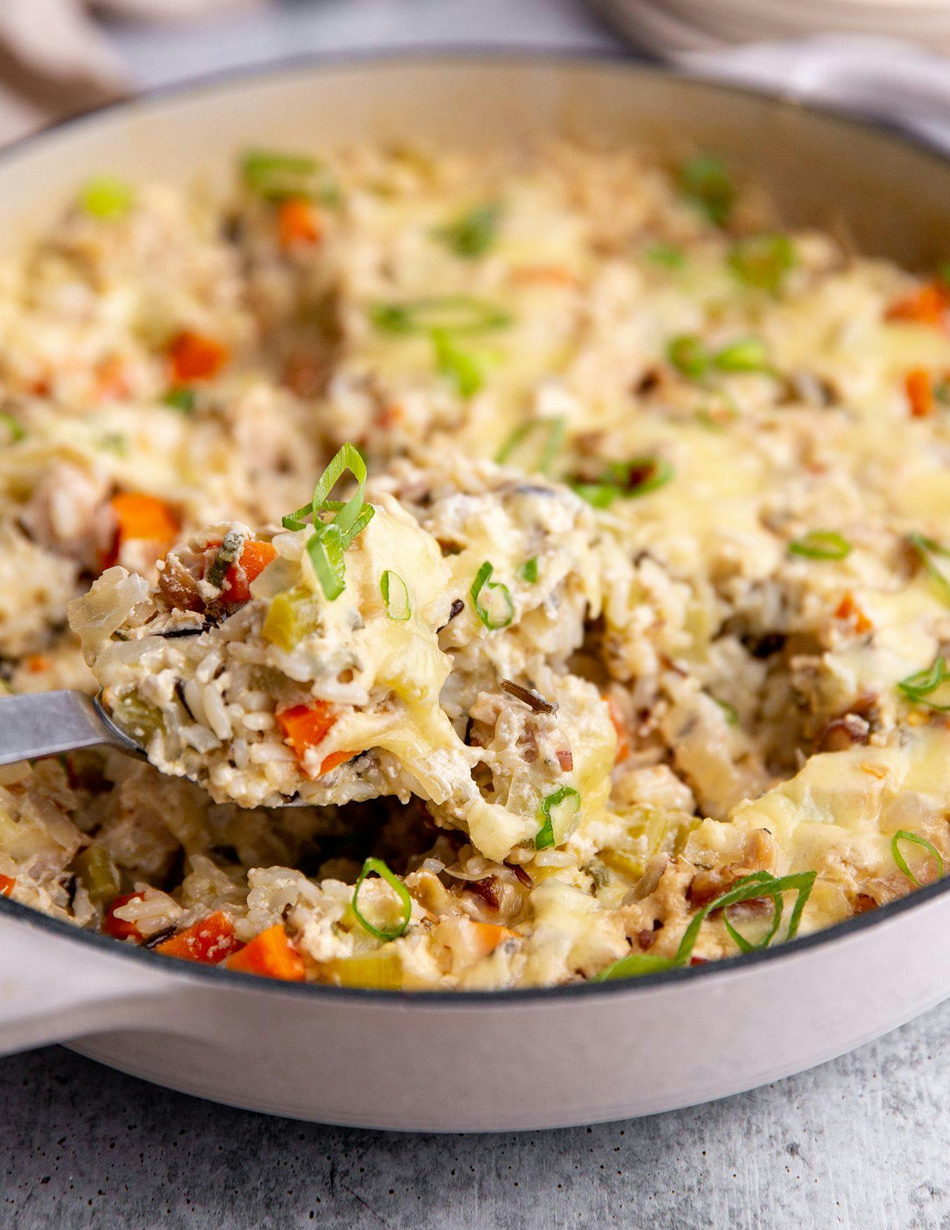 A pan of cheesy chicken and wild rice casserole with a spoon in it. 