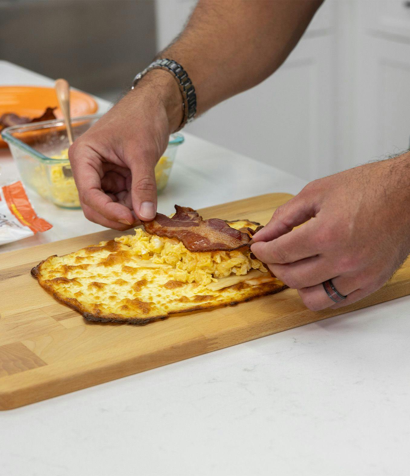 A man puts bacon and scrambled eggs on cottage cheese bread.