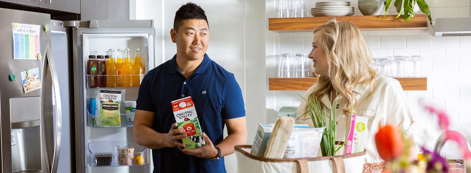 Man and woman holding carton of milk in kitchen with other groceries.