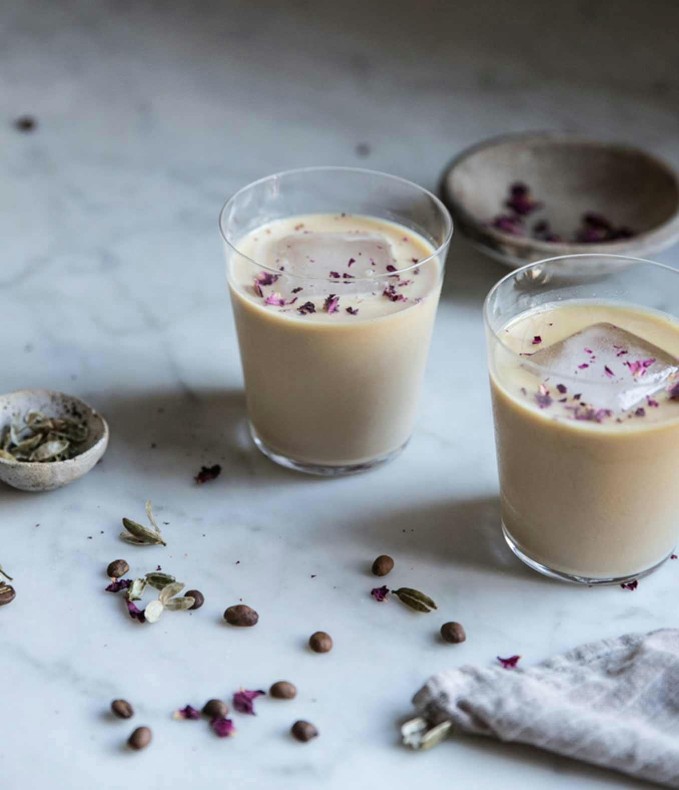 Cardamom Rose Lattes in two glasses with a large ice cube in each one.