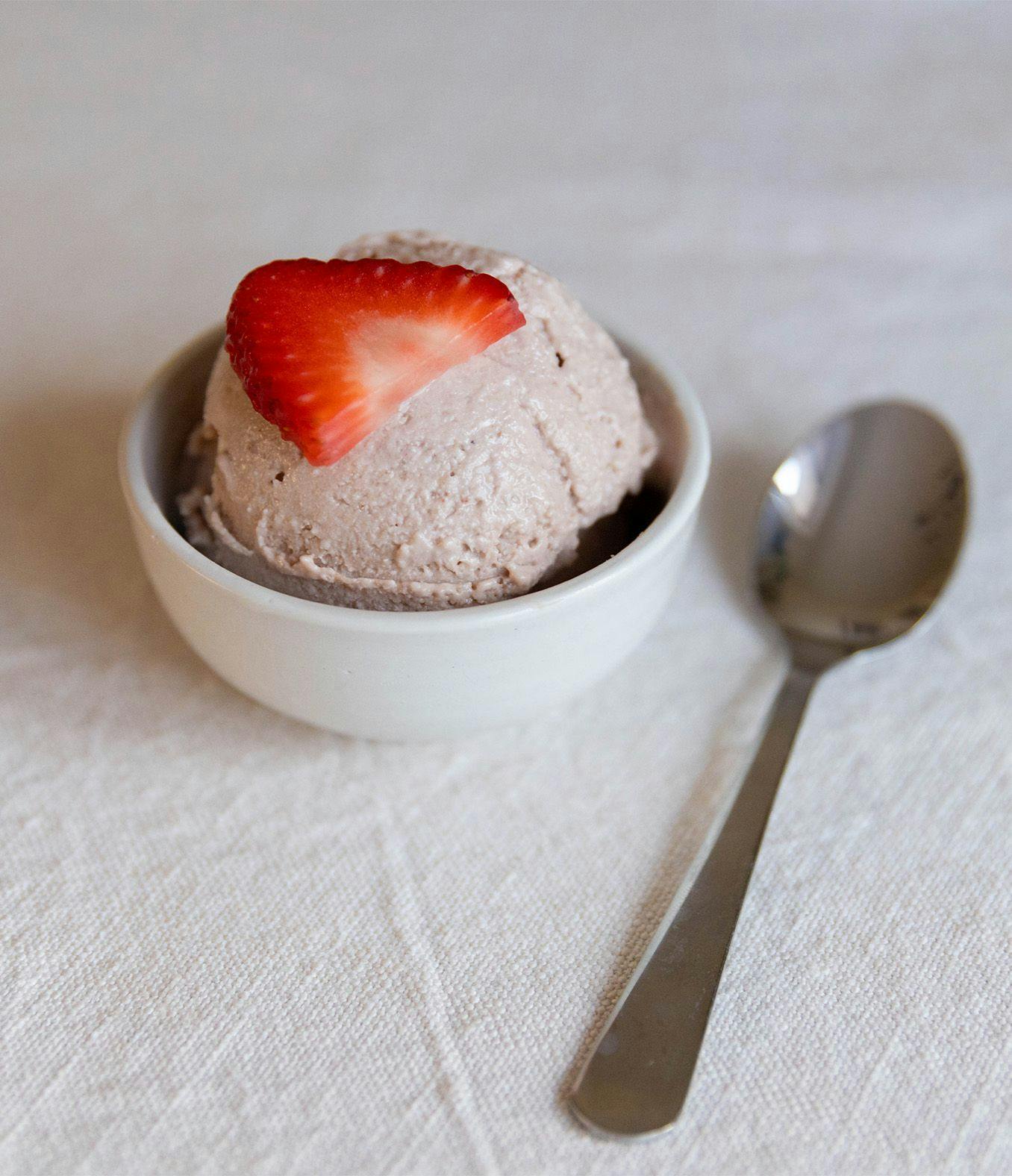 Scoop of cottage cheese ice cream in a dish with a fresh strawberry and spoon.