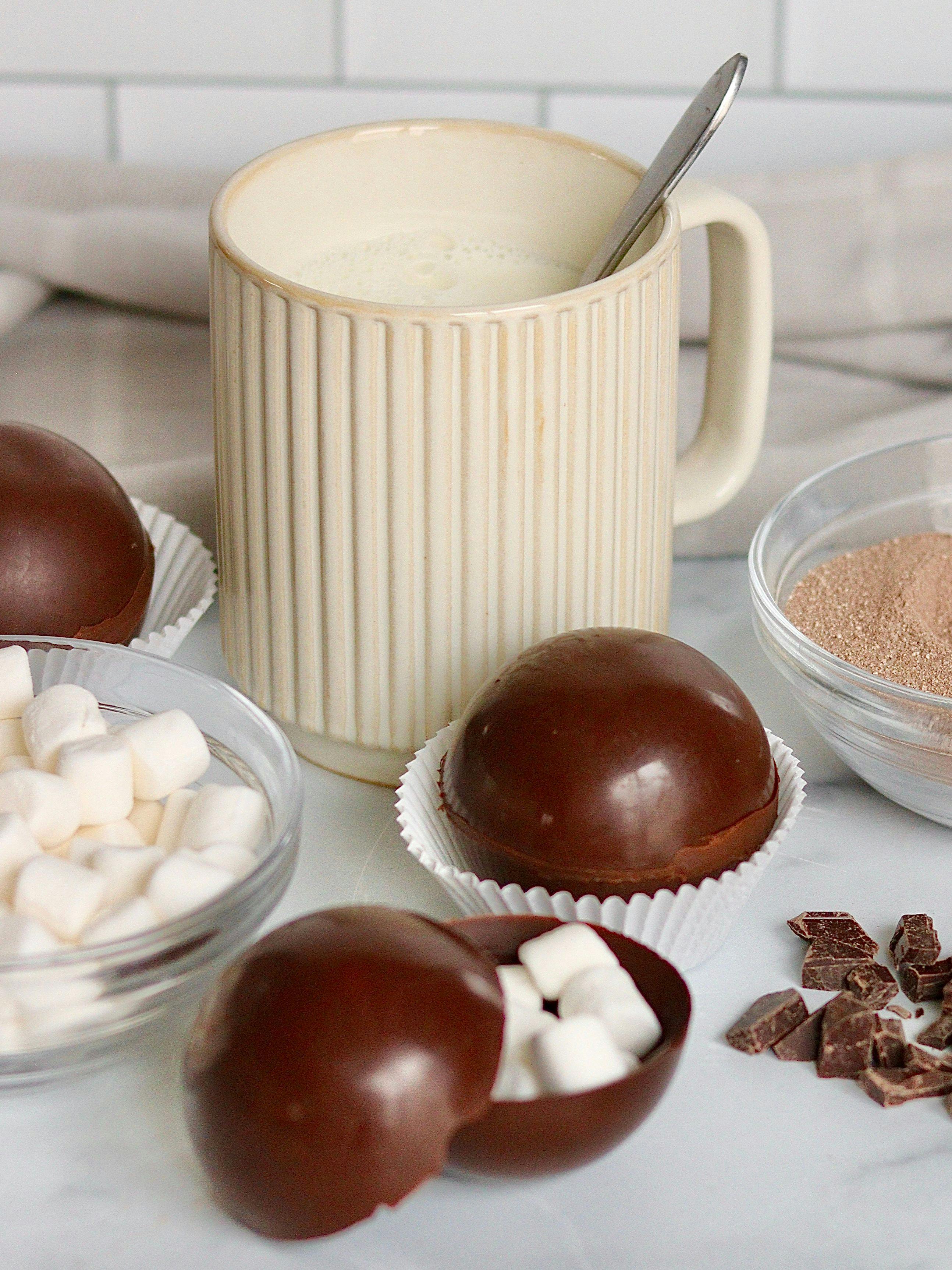 Hot chocolate bombs on a counter with ingredients and marshmallows.
