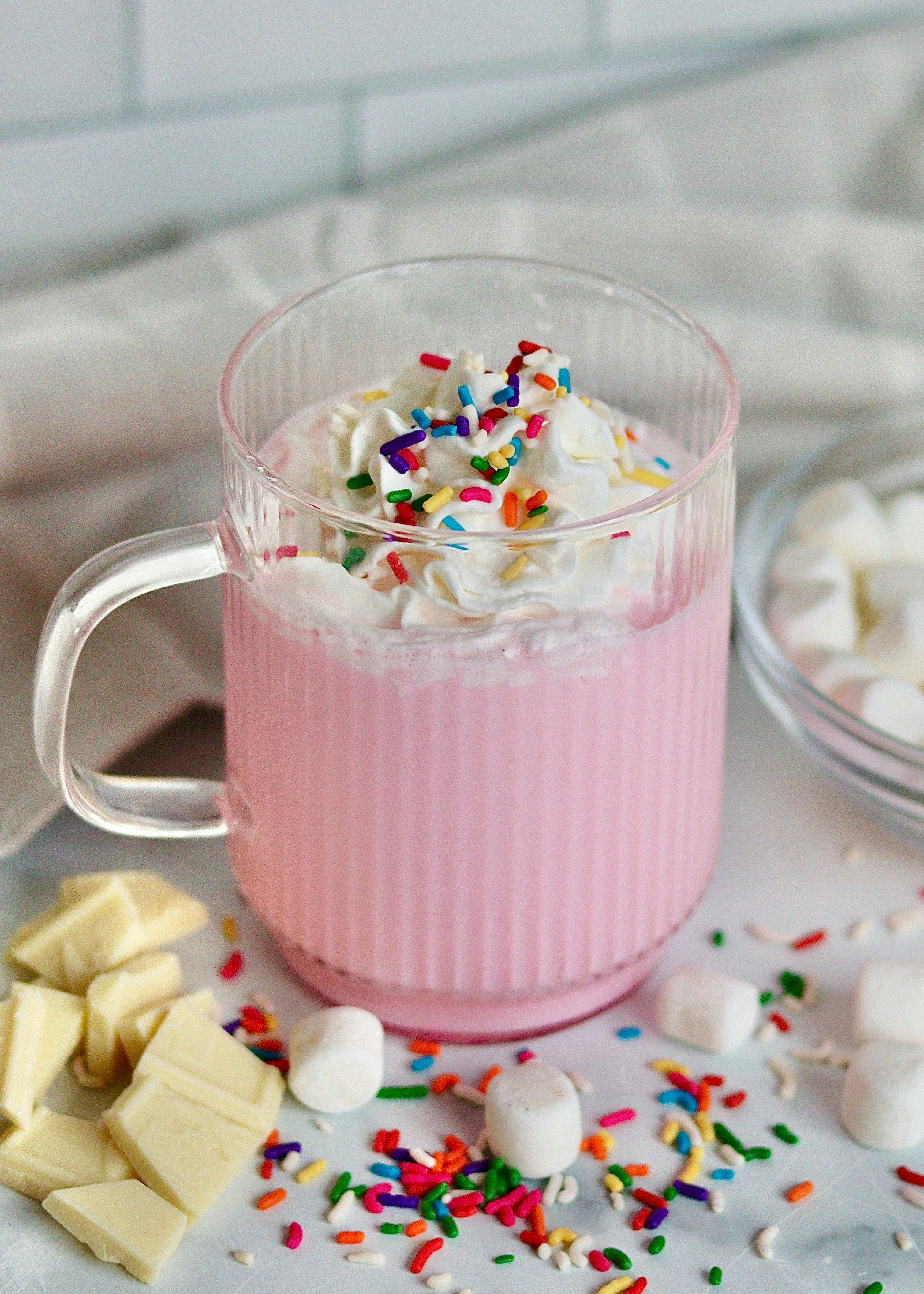 A mug of pink unicorn hot chocolate with marshmallows, sprinkles and whipped cream.