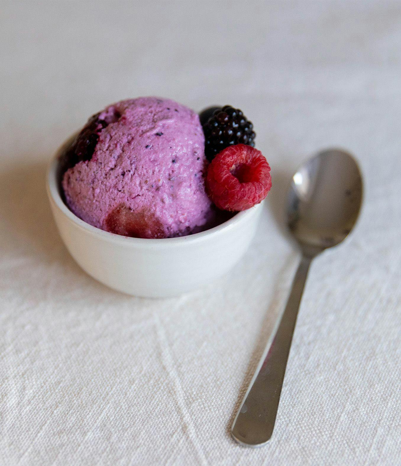 Scoop of cottage cheese ice cream in a dish with fresh berries and spoon.