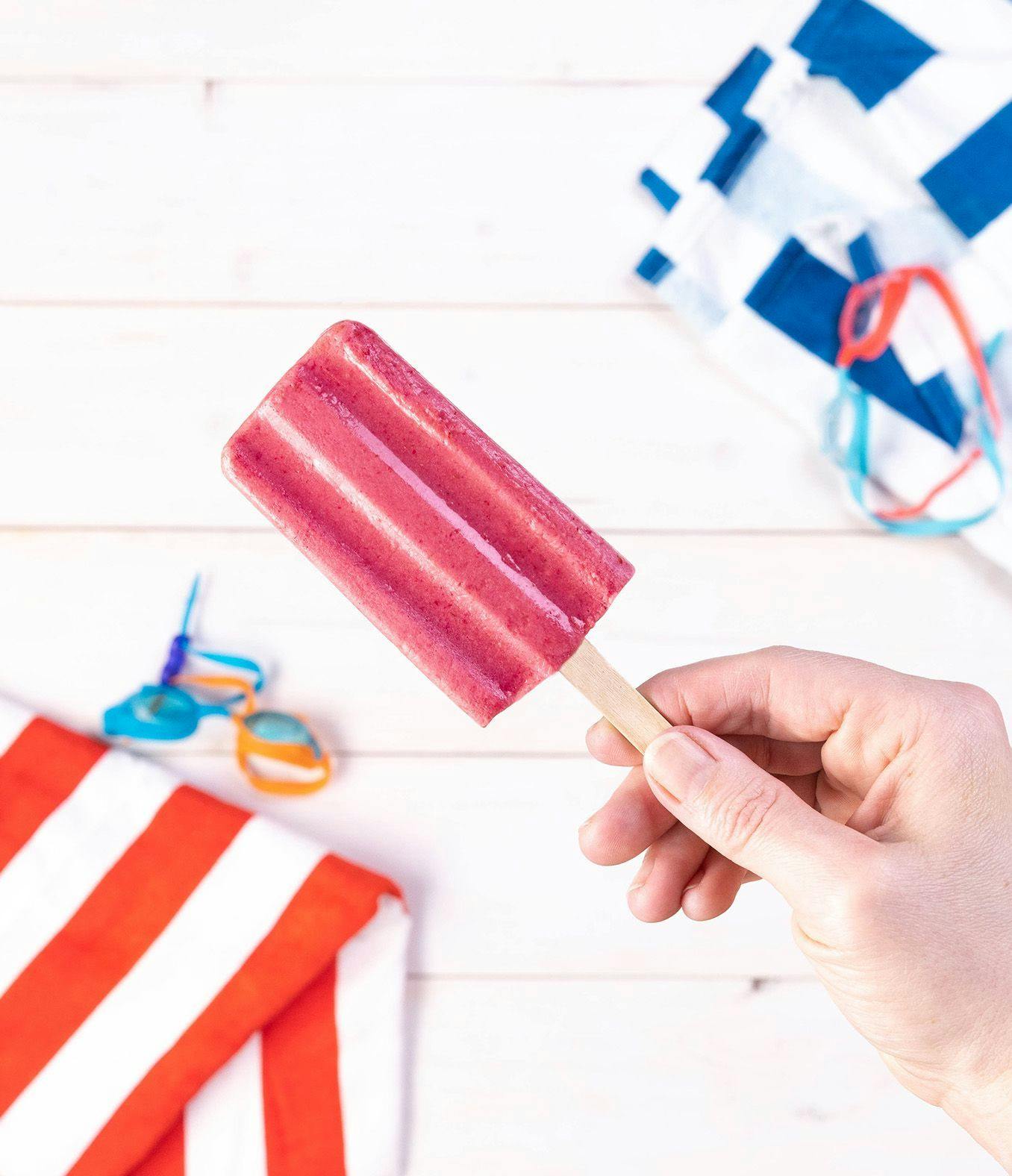 Hand holding a Creamy Raspberry Popsicle next to pool towels.